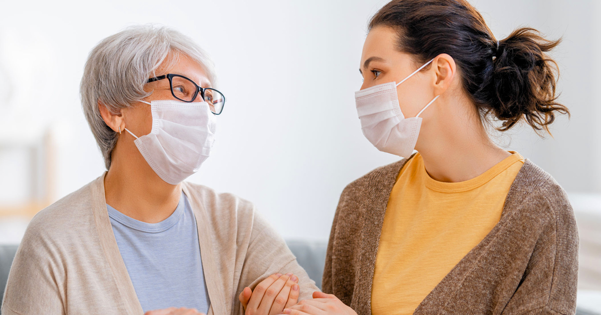 Masked senior woman talking with masked daughter.