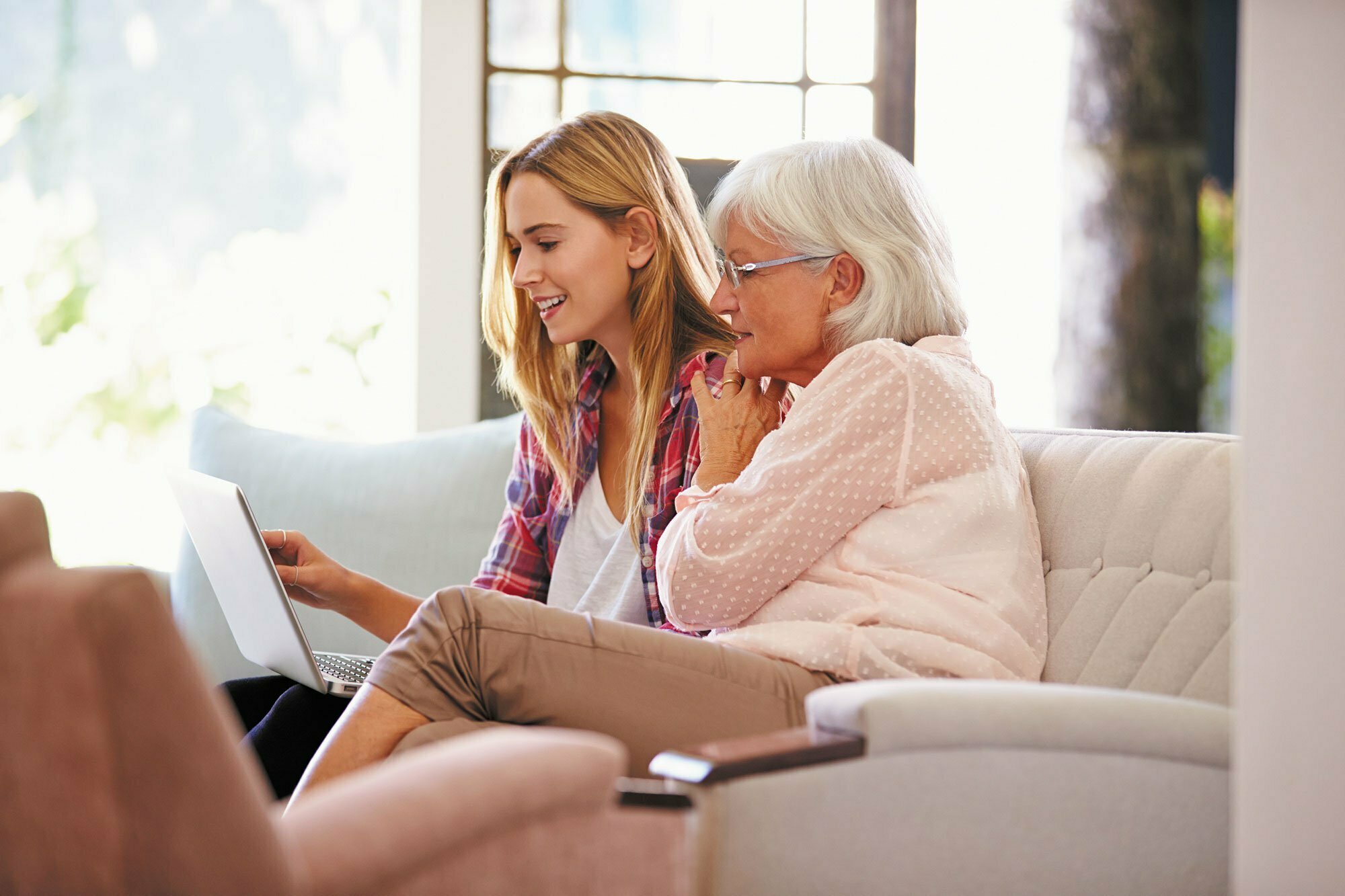 Woman and daughter work on laptop in living room.