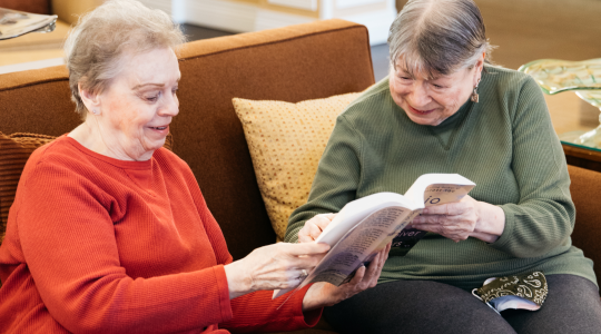Two Ladies sitting on couch holding book together