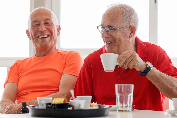 two older men laughing and drinking coffee